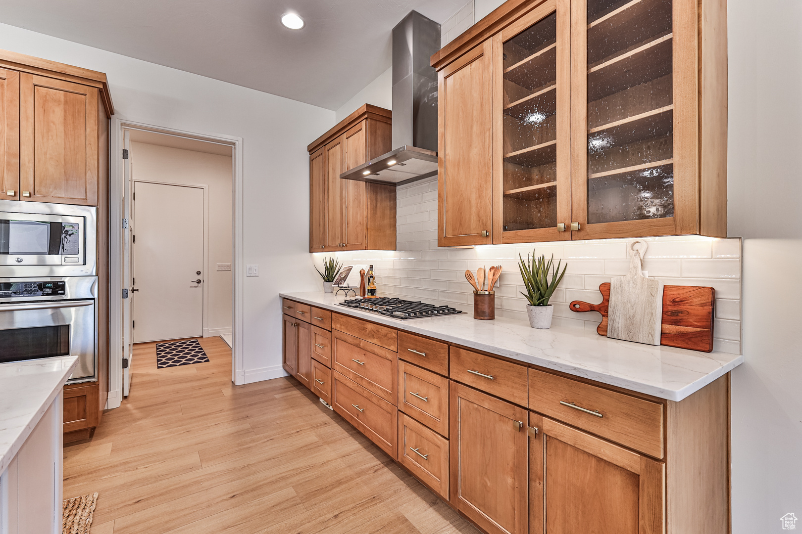 Kitchen featuring light hardwood / wood-style flooring, backsplash, wall chimney range hood, stainless steel appliances, and light stone countertops
