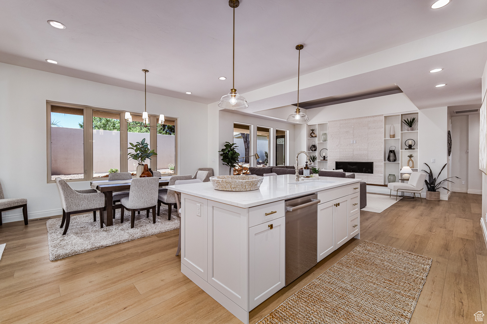 Kitchen featuring a center island with sink, light wood-type flooring, white cabinetry, decorative light fixtures, and stainless steel dishwasher