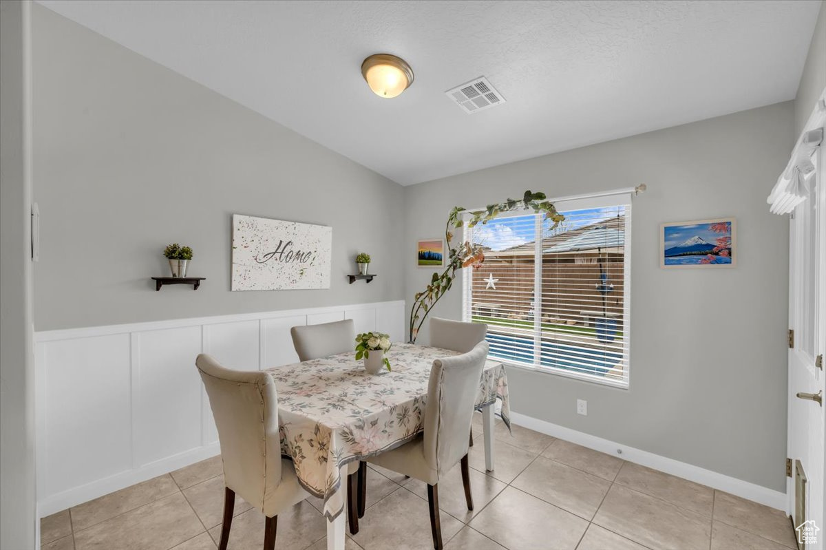 Dining area with a wainscoted wall, visible vents, a decorative wall, and light tile patterned flooring
