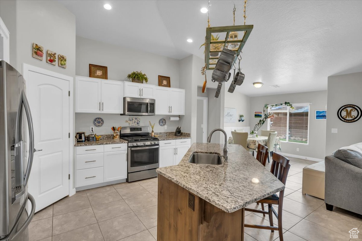 Kitchen with a center island with sink, white cabinets, appliances with stainless steel finishes, light stone countertops, and a sink
