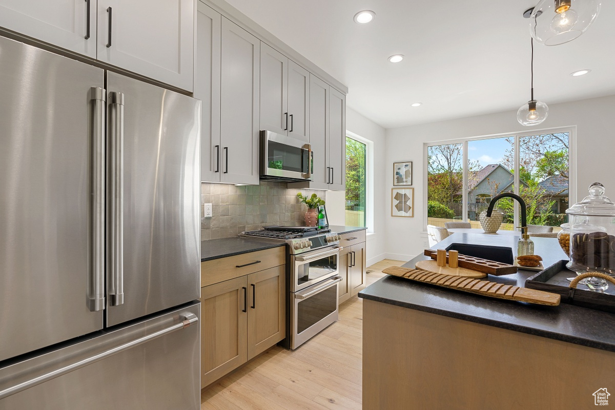Kitchen featuring stainless steel appliances, hanging light fixtures, dark countertops, and decorative backsplash