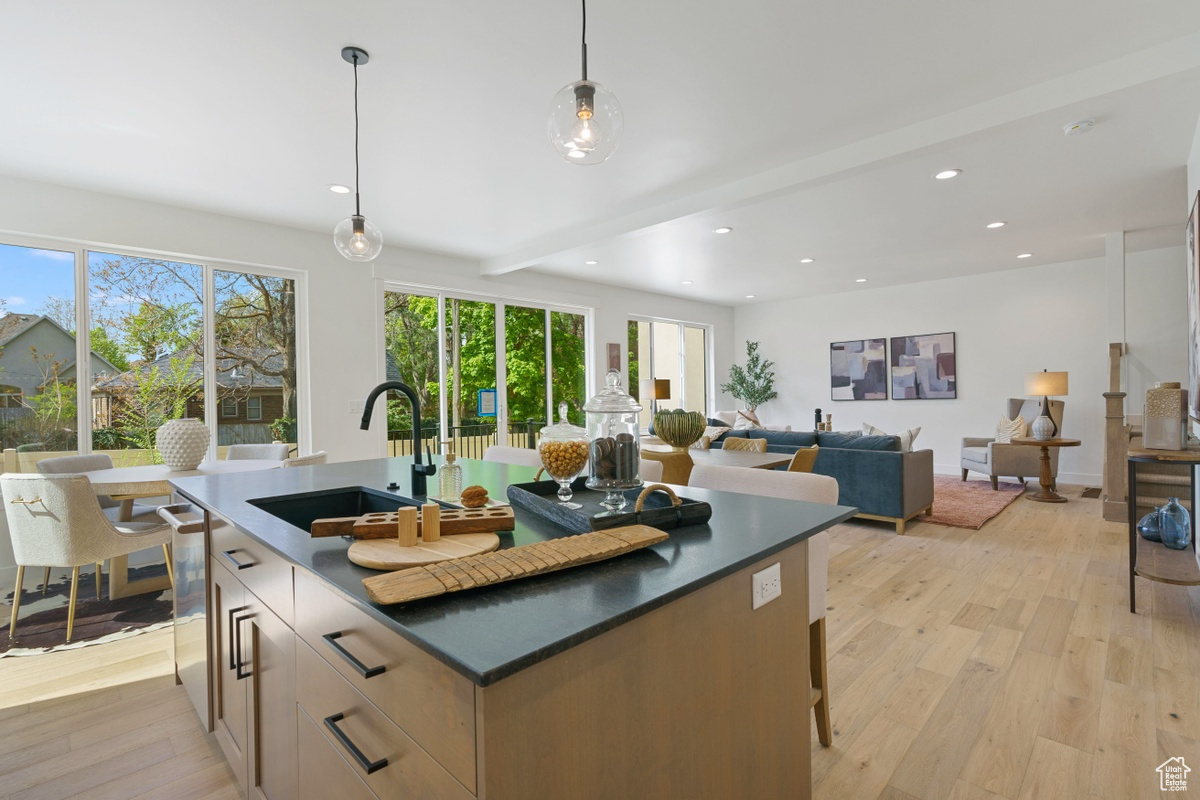 Kitchen with decorative light fixtures, dark countertops, open floor plan, a sink, and an island with sink