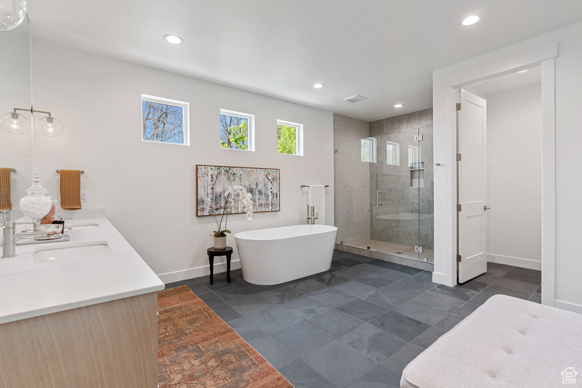 Full bath with double vanity, recessed lighting, a soaking tub, a stall shower, and baseboards