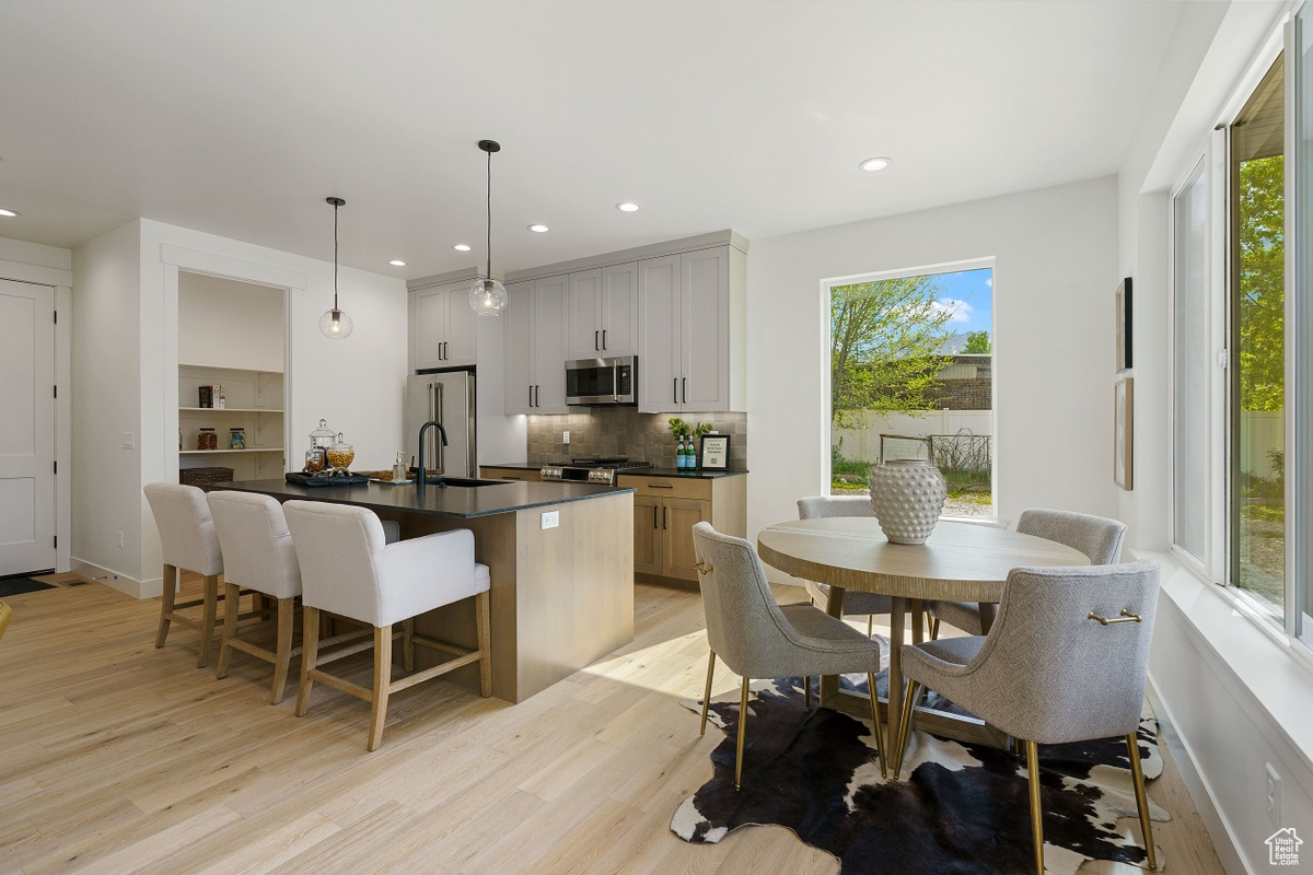 Kitchen with a center island with sink, stainless steel appliances, dark countertops, hanging light fixtures, and white cabinetry