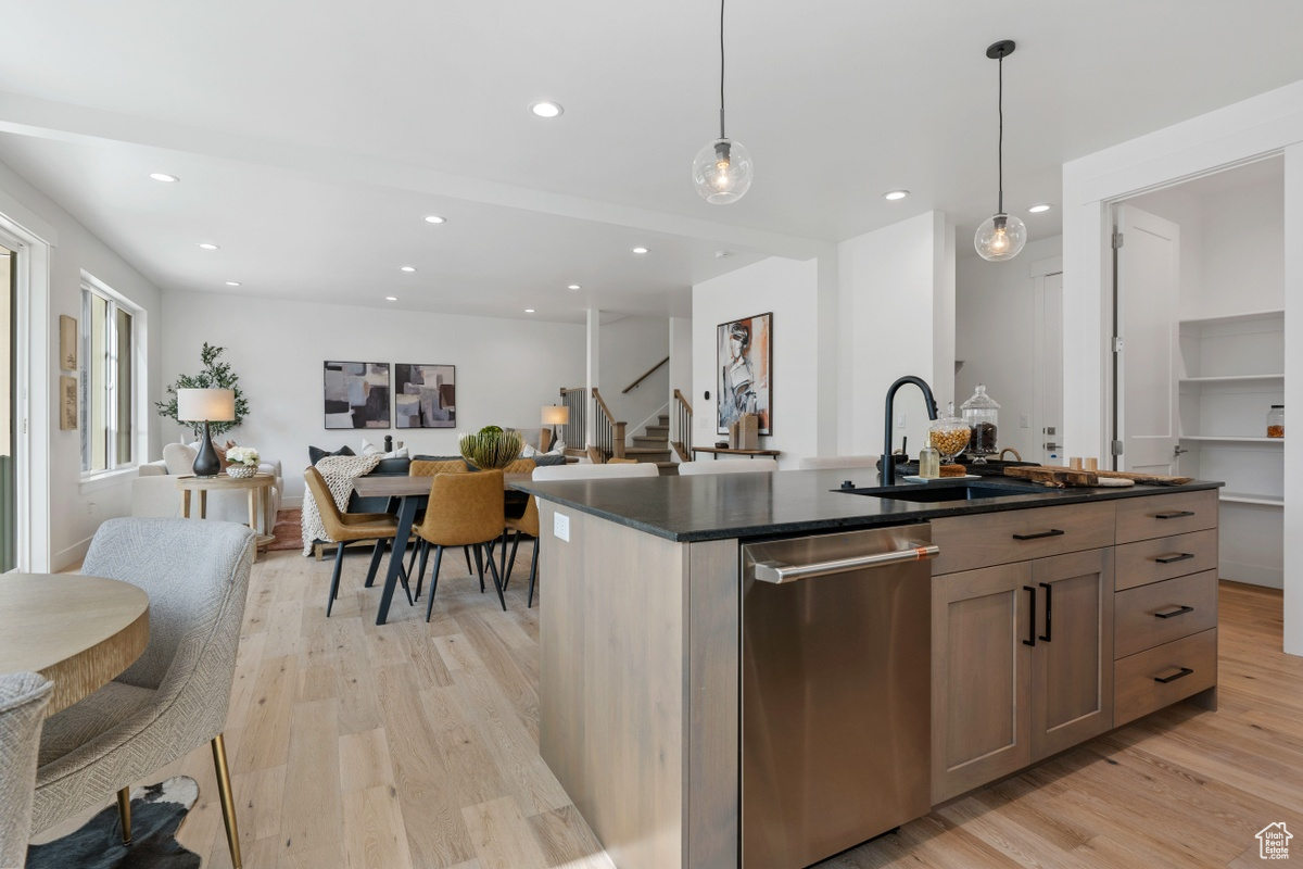 Kitchen with pendant lighting, a center island with sink, dark countertops, open floor plan, and dishwasher