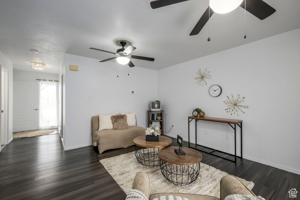 Living area with dark wood finished floors, a ceiling fan, and baseboards