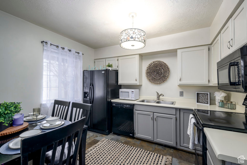 Kitchen featuring stone finish floor, gray cabinets, light countertops, black appliances, and a sink