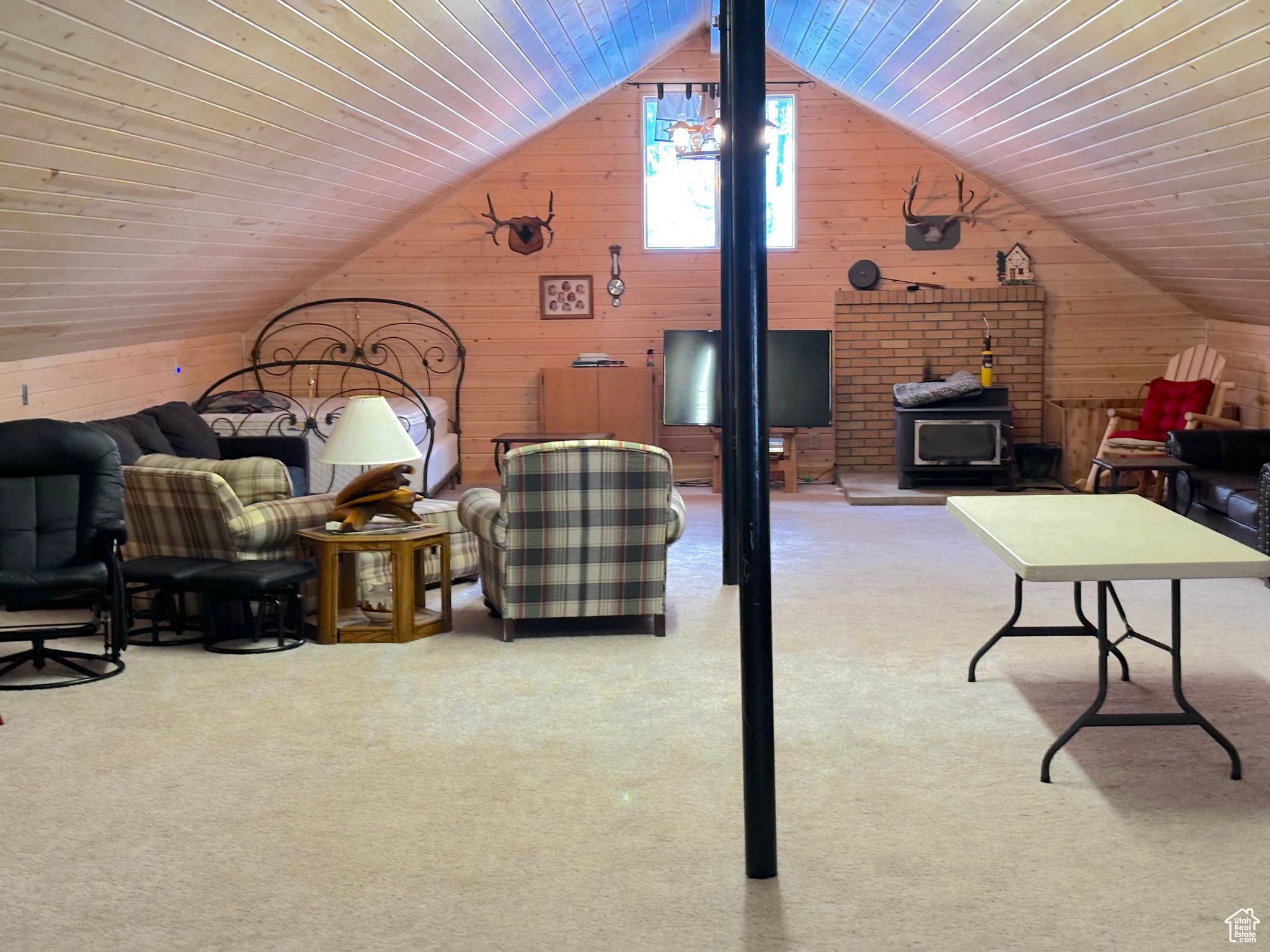 Interior space featuring lofted ceiling, a wood stove, light carpet, and wooden walls