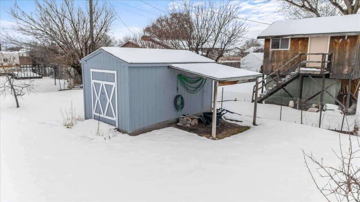 Snow covered structure with a shed and fence