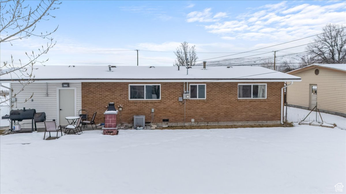 Snow covered rear of property with brick siding and central air condition unit