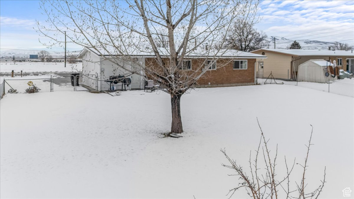Snow covered back of property featuring an outbuilding, brick siding, fence, and a storage shed
