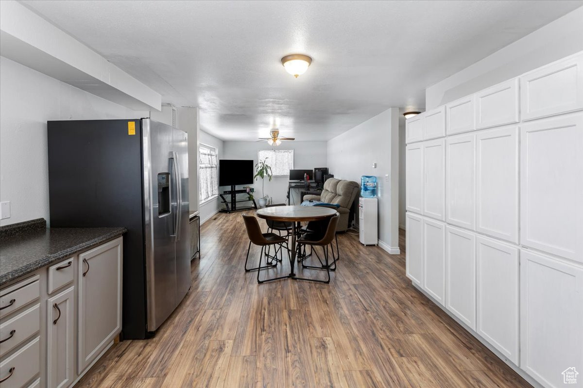Kitchen with dark wood-style flooring, white cabinets, open floor plan, dark countertops, and stainless steel fridge