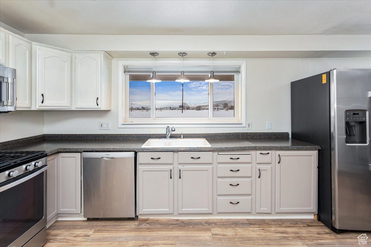 Kitchen featuring a sink, white cabinetry, hanging light fixtures, appliances with stainless steel finishes, and dark countertops