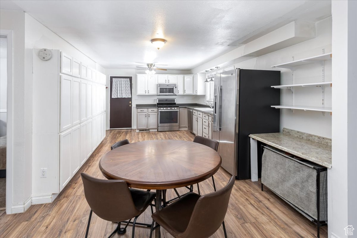 Kitchen with appliances with stainless steel finishes, a ceiling fan, white cabinetry, a sink, and wood finished floors