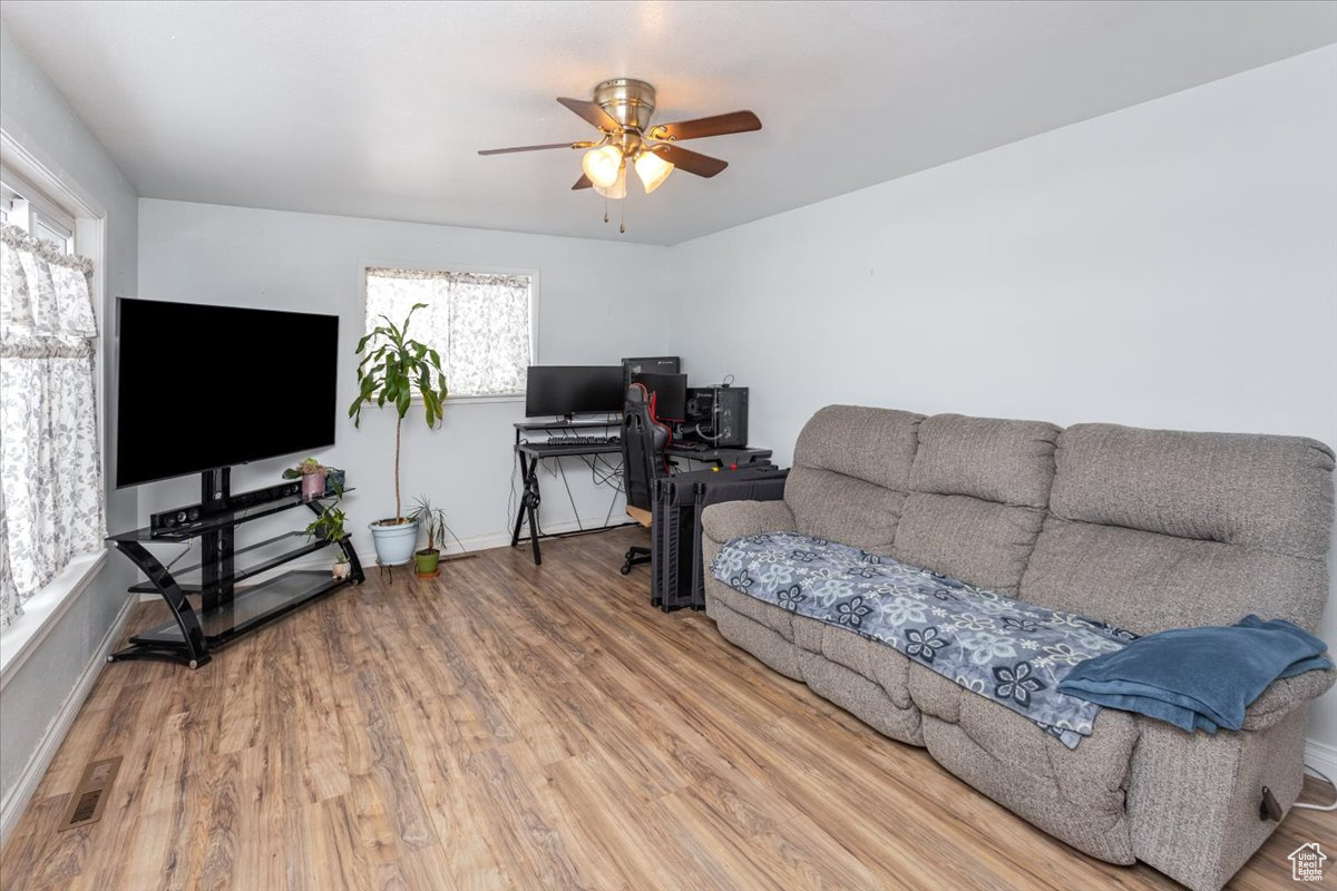 Living room with a ceiling fan, visible vents, baseboards, and wood finished floors