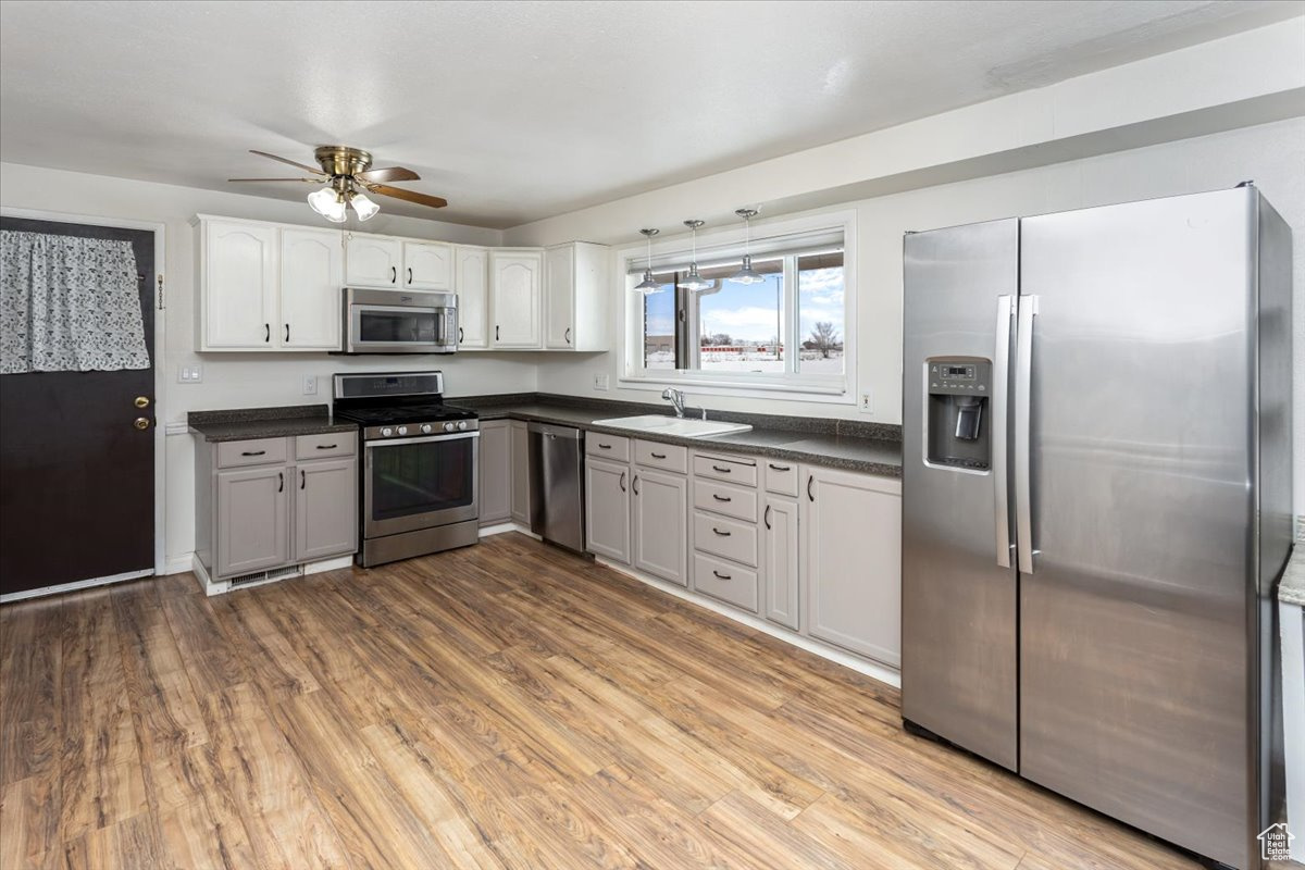 Kitchen with dark countertops, light wood-type flooring, appliances with stainless steel finishes, and a sink