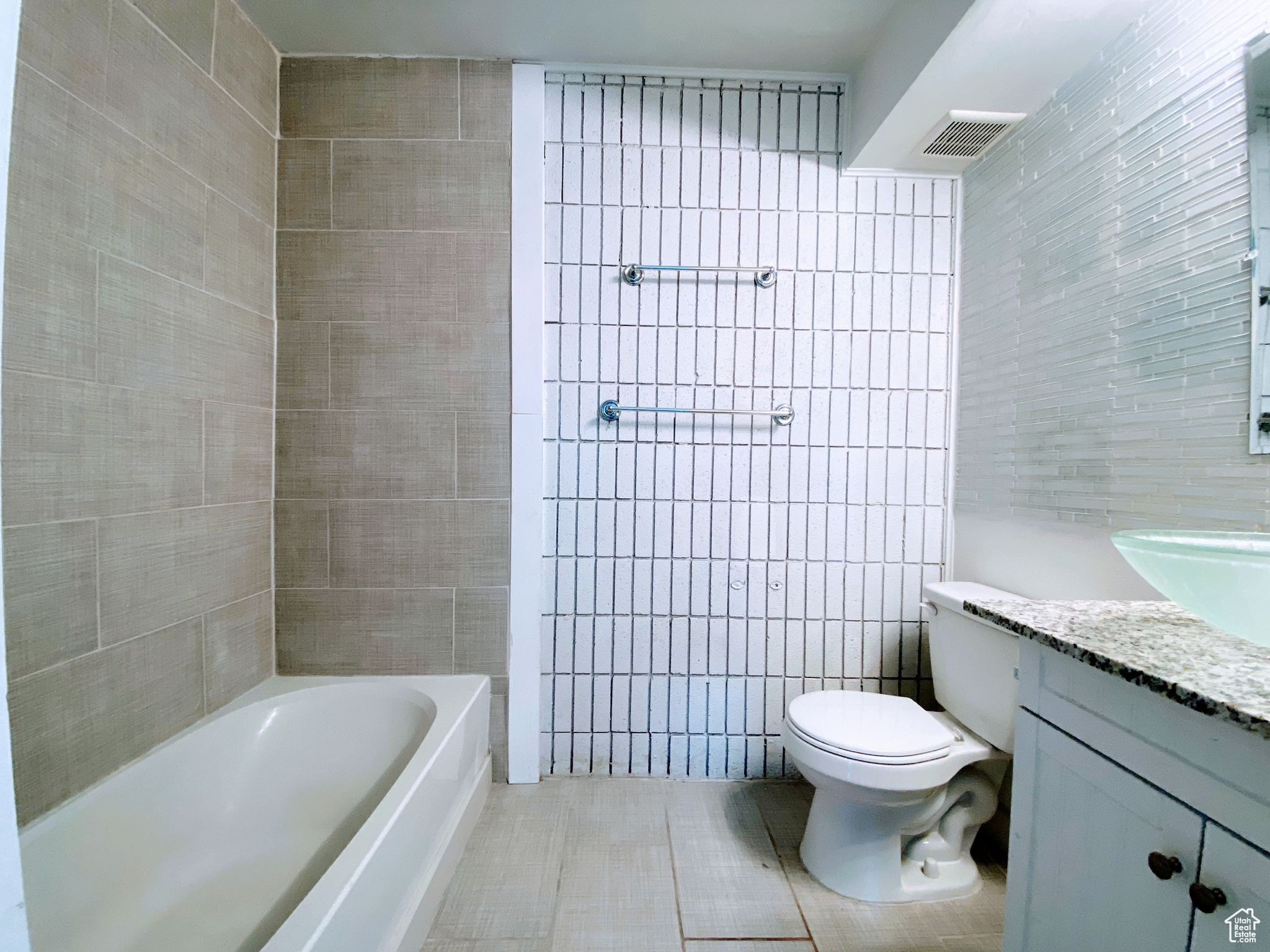Bathroom featuring tile patterned flooring, toilet, a bathing tub, vanity, and tile walls