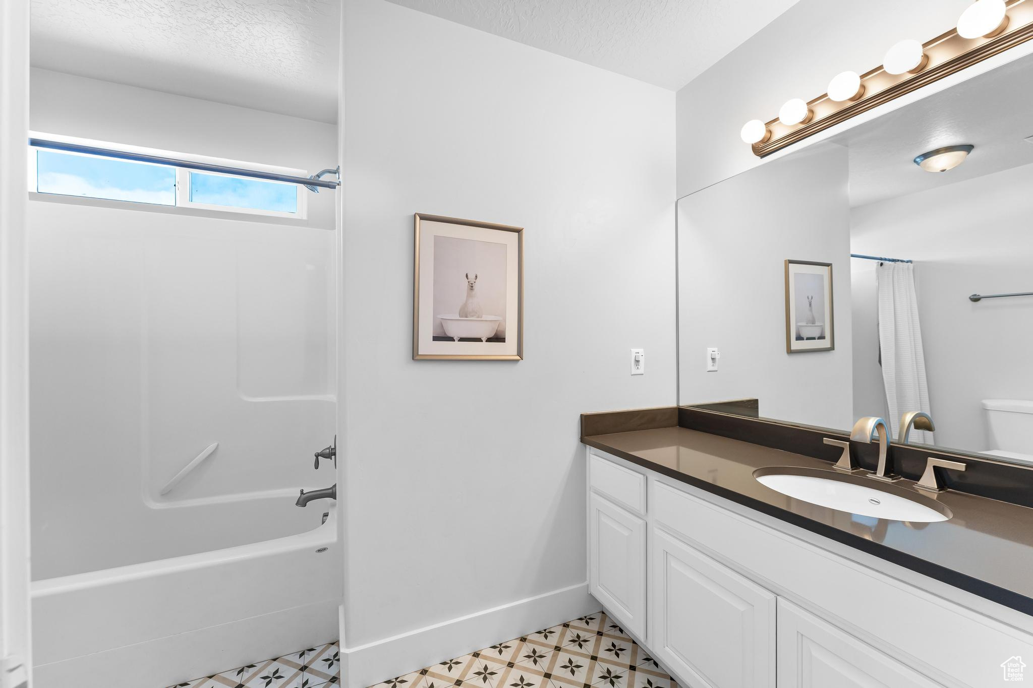 Full bathroom featuring a textured ceiling, vanity, baseboards, tile patterned floors, and shower / bath combo