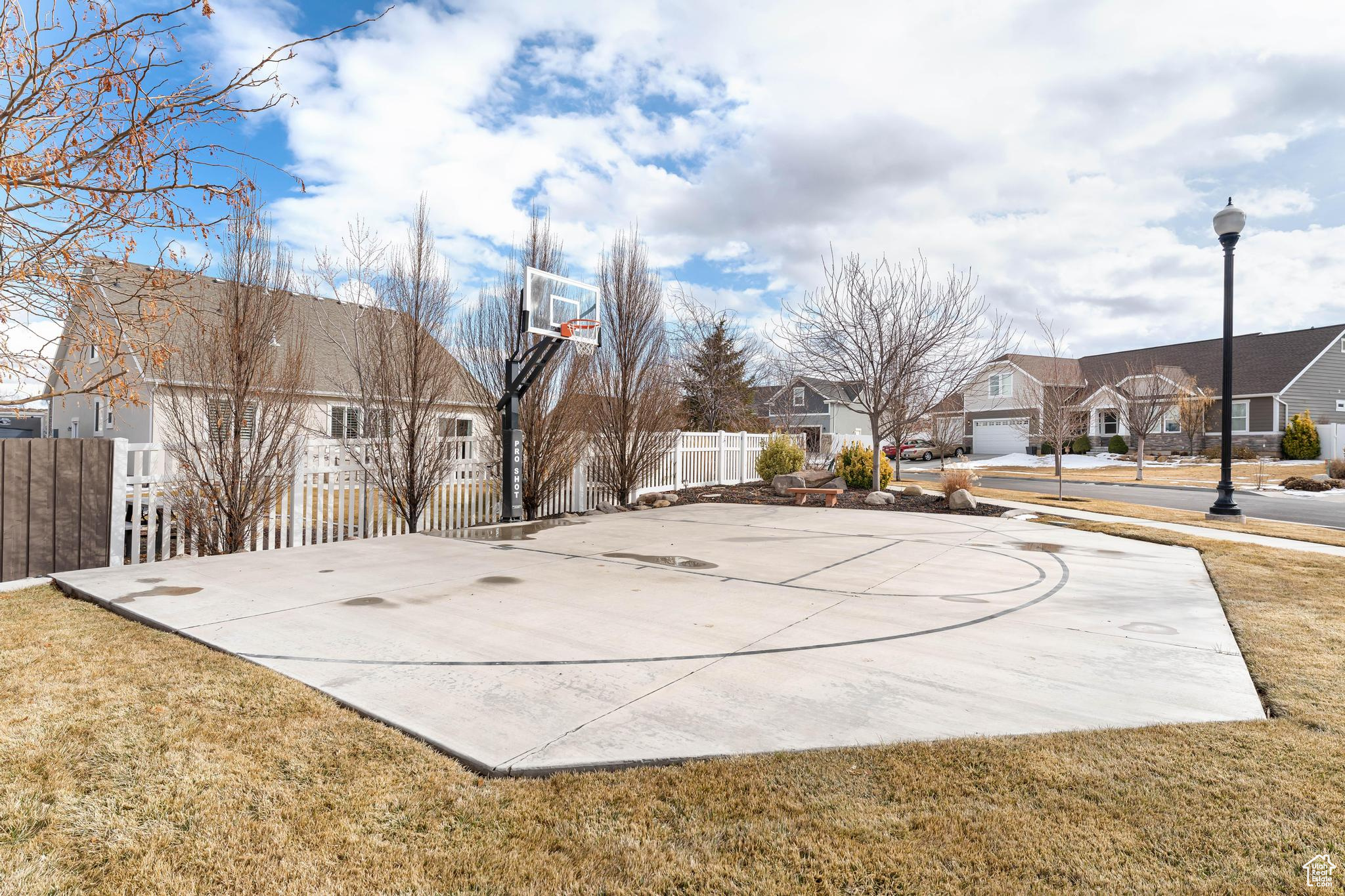 View of sport court with basketball hoop, a residential view, fence, and a yard