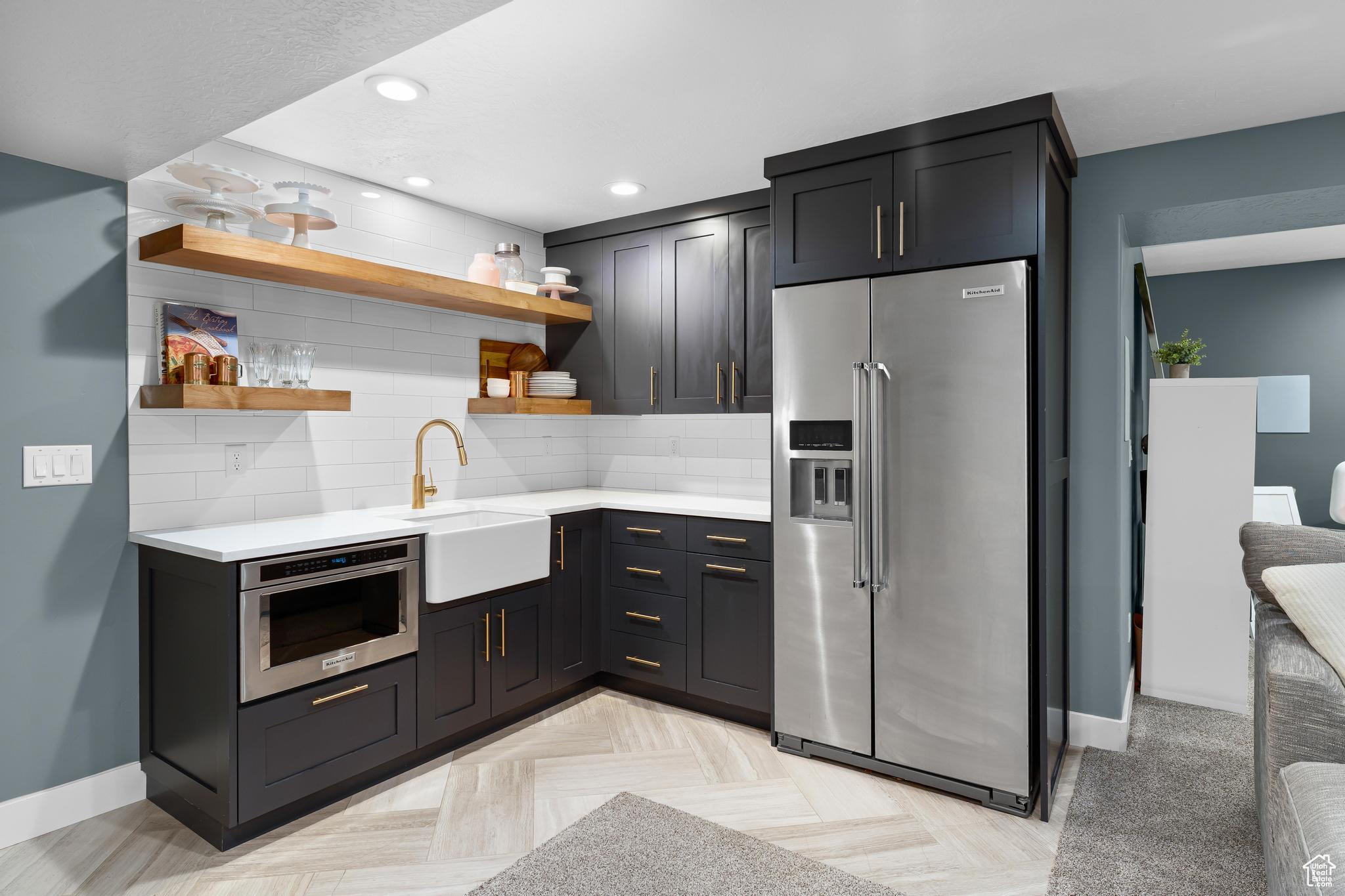 Kitchen with high end refrigerator, a sink, light countertops, decorative backsplash, and open shelves