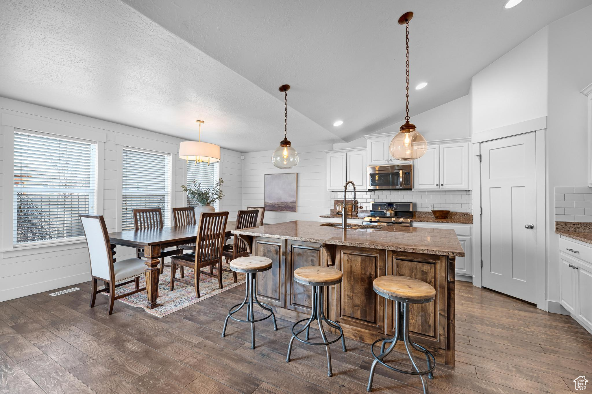 Kitchen featuring pendant lighting, light stone counters, a center island with sink, and white cabinets
