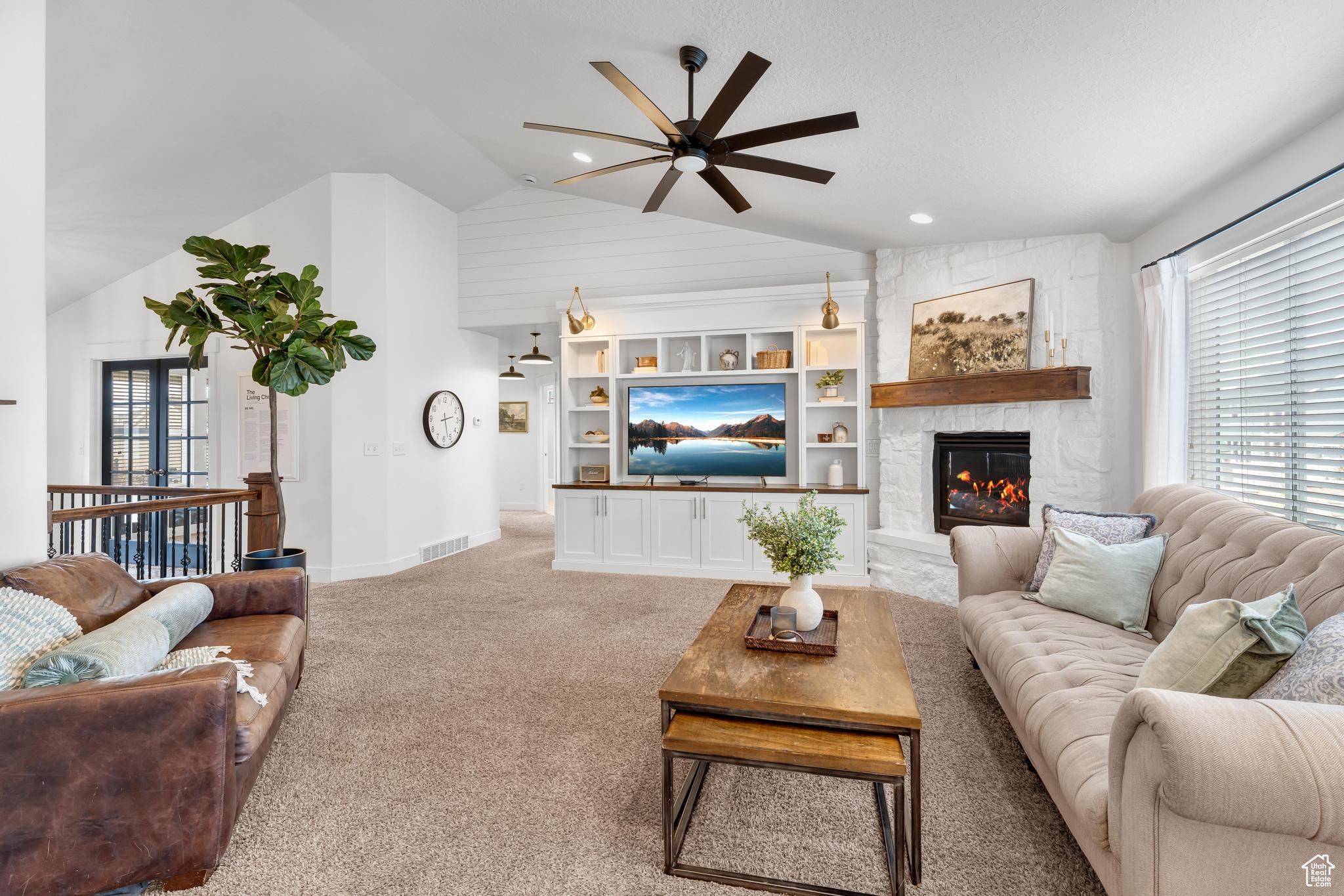 Carpeted living room featuring ceiling fan, high vaulted ceiling, a stone fireplace, recessed lighting and built in cabinets