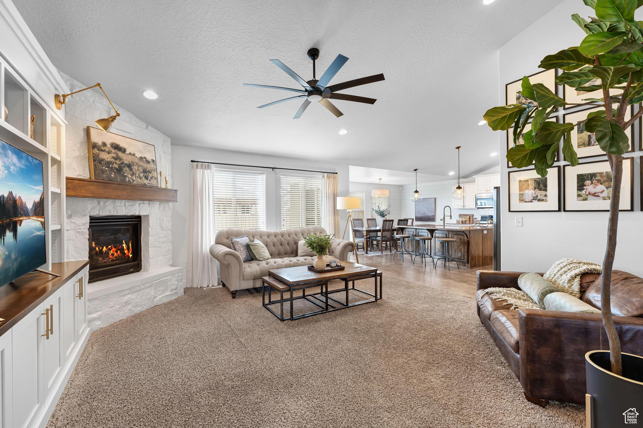 Living room featuring lofted ceiling, ceiling fan, a textured ceiling, and a stone fireplace