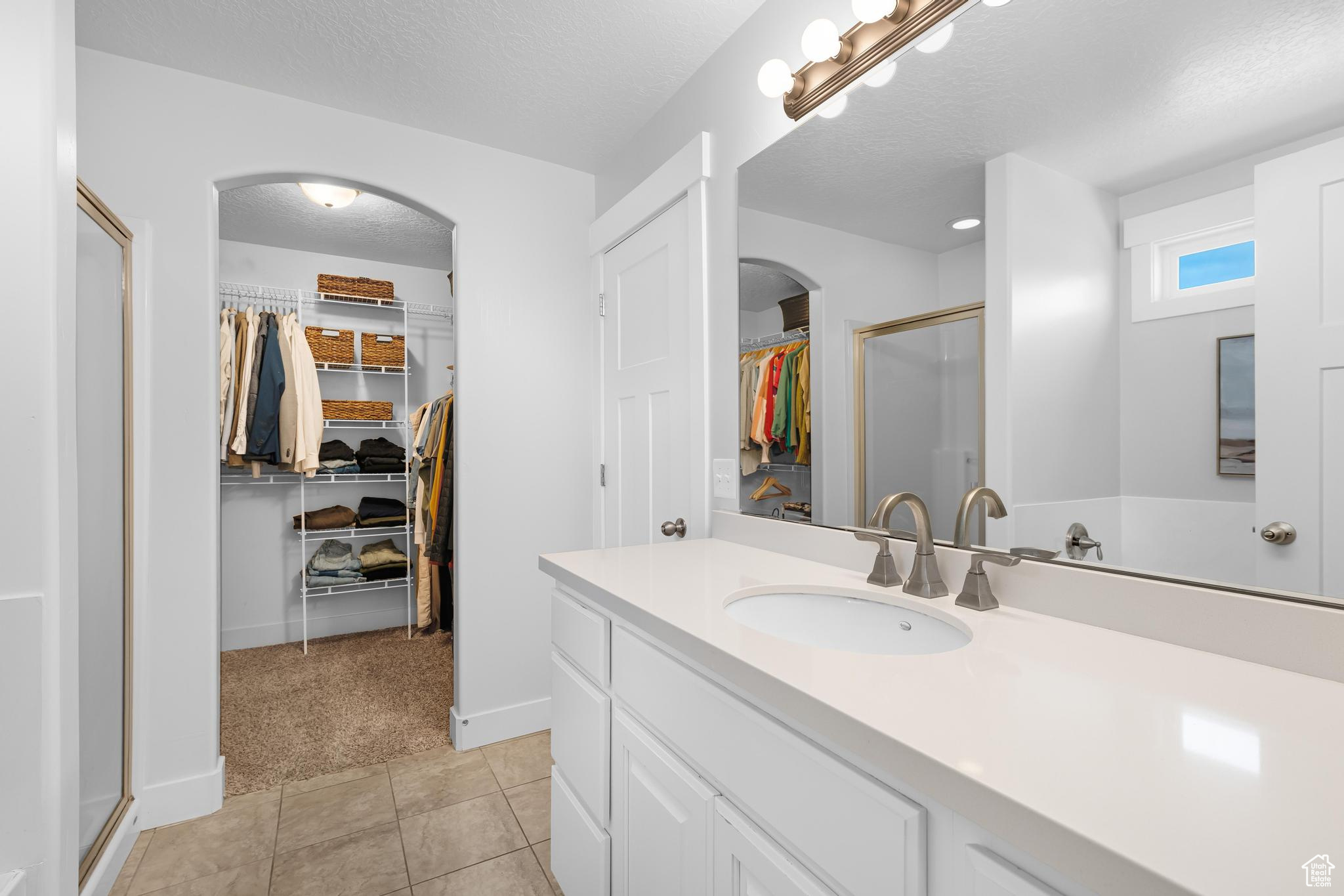 Bathroom with a textured ceiling, tile patterned flooring, a walk in closet, and a shower stall