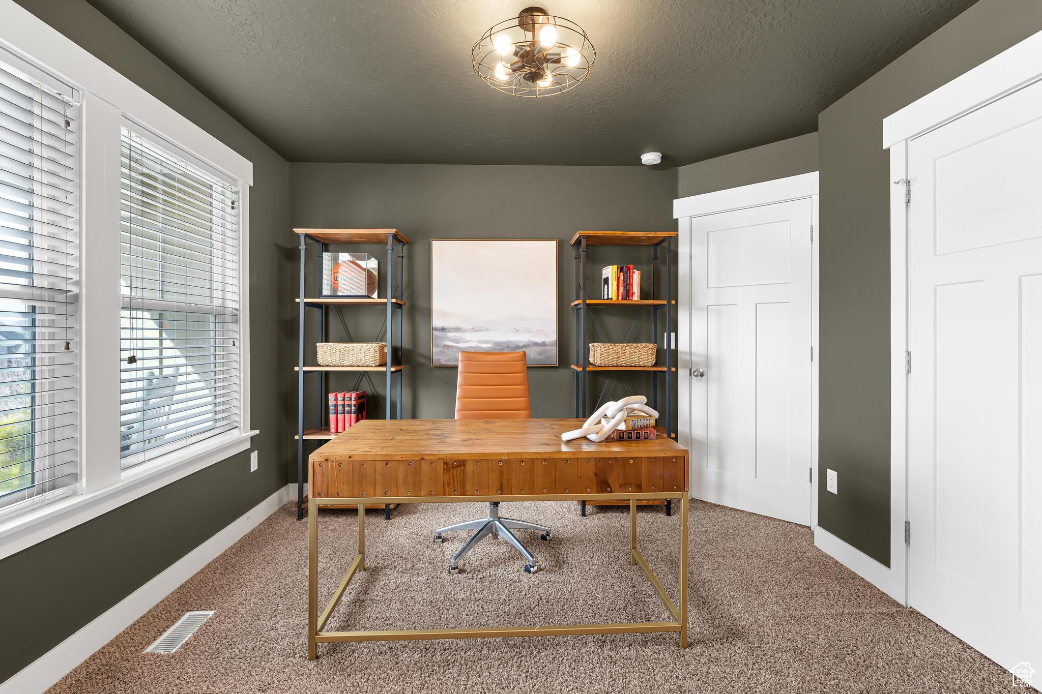Carpeted home office featuring a notable chandelier