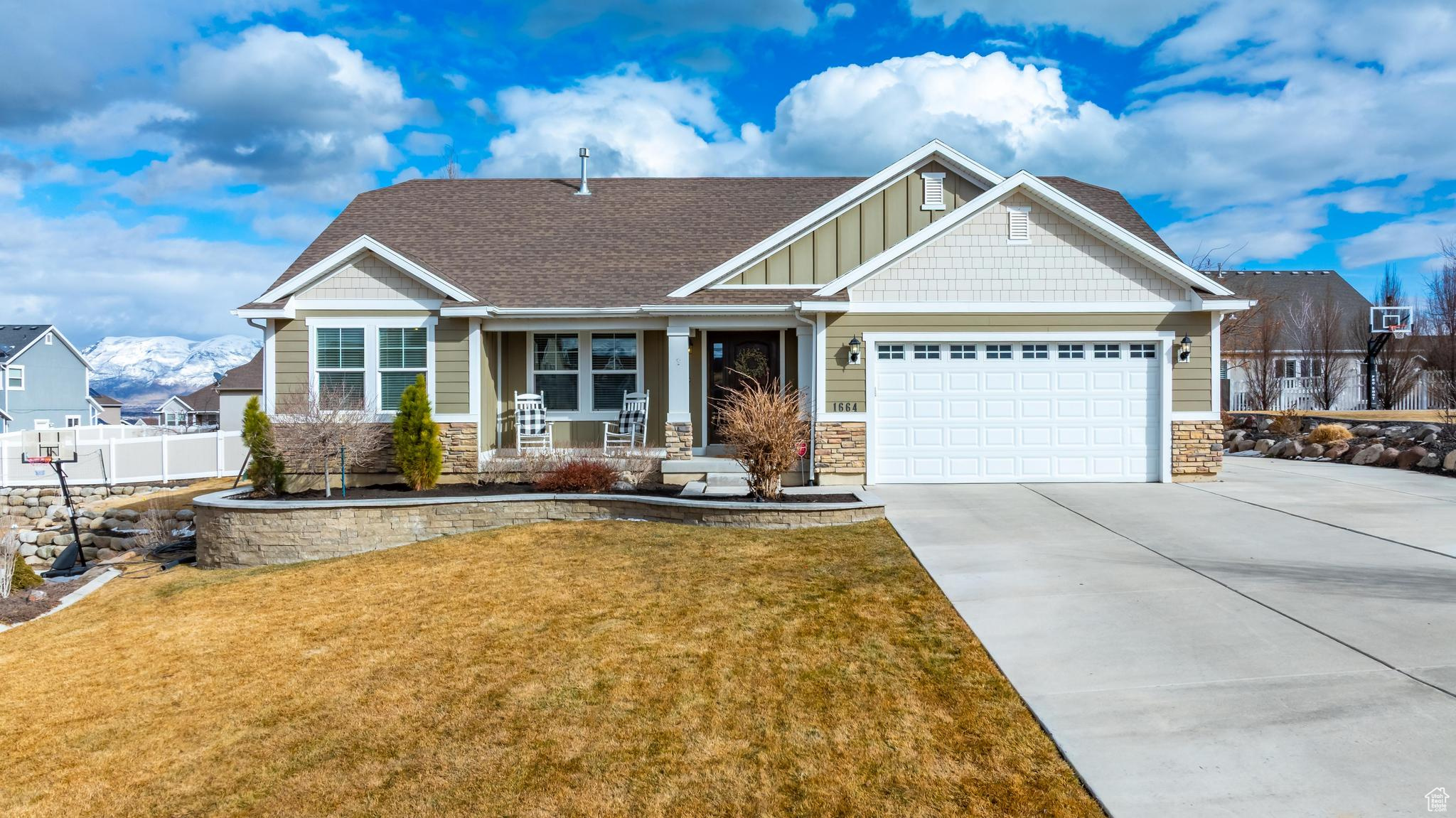Craftsman-style home featuring driveway, stone siding, fence, a front lawn, and board and batten siding