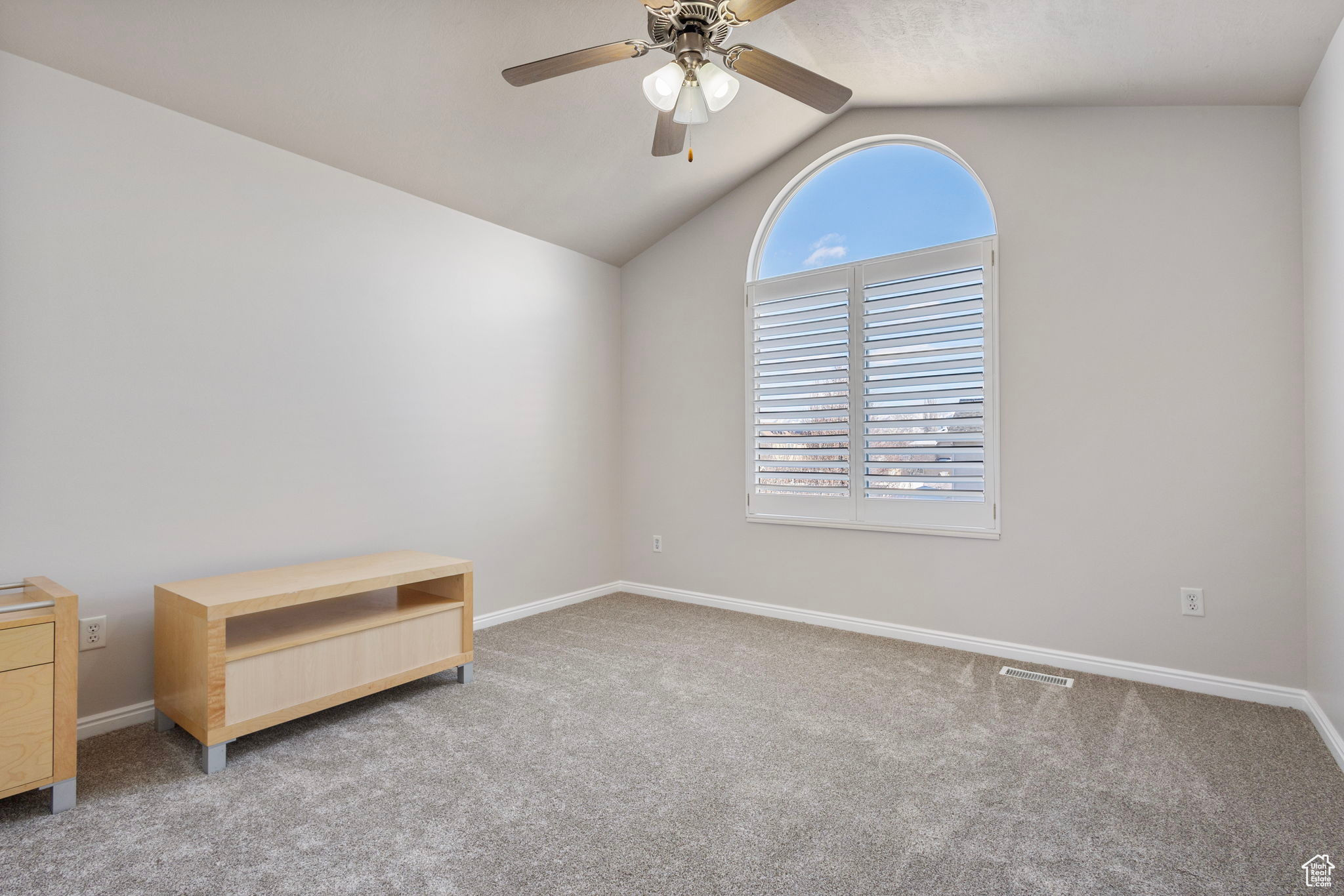 Carpeted spare room with ceiling fan and vaulted ceiling