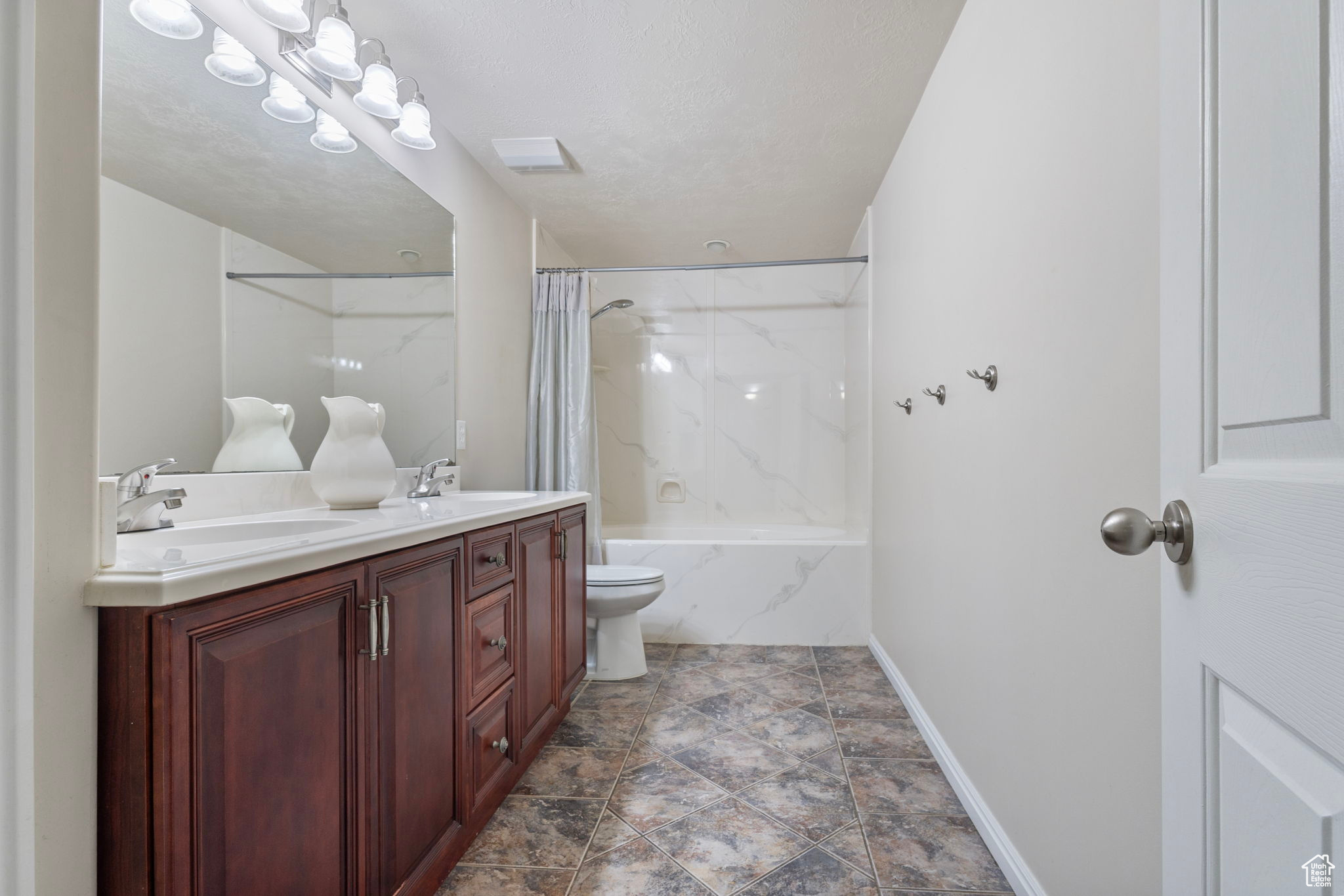 Full bathroom with a textured ceiling, vanity, toilet, and shower / bathtub combination with curtain
