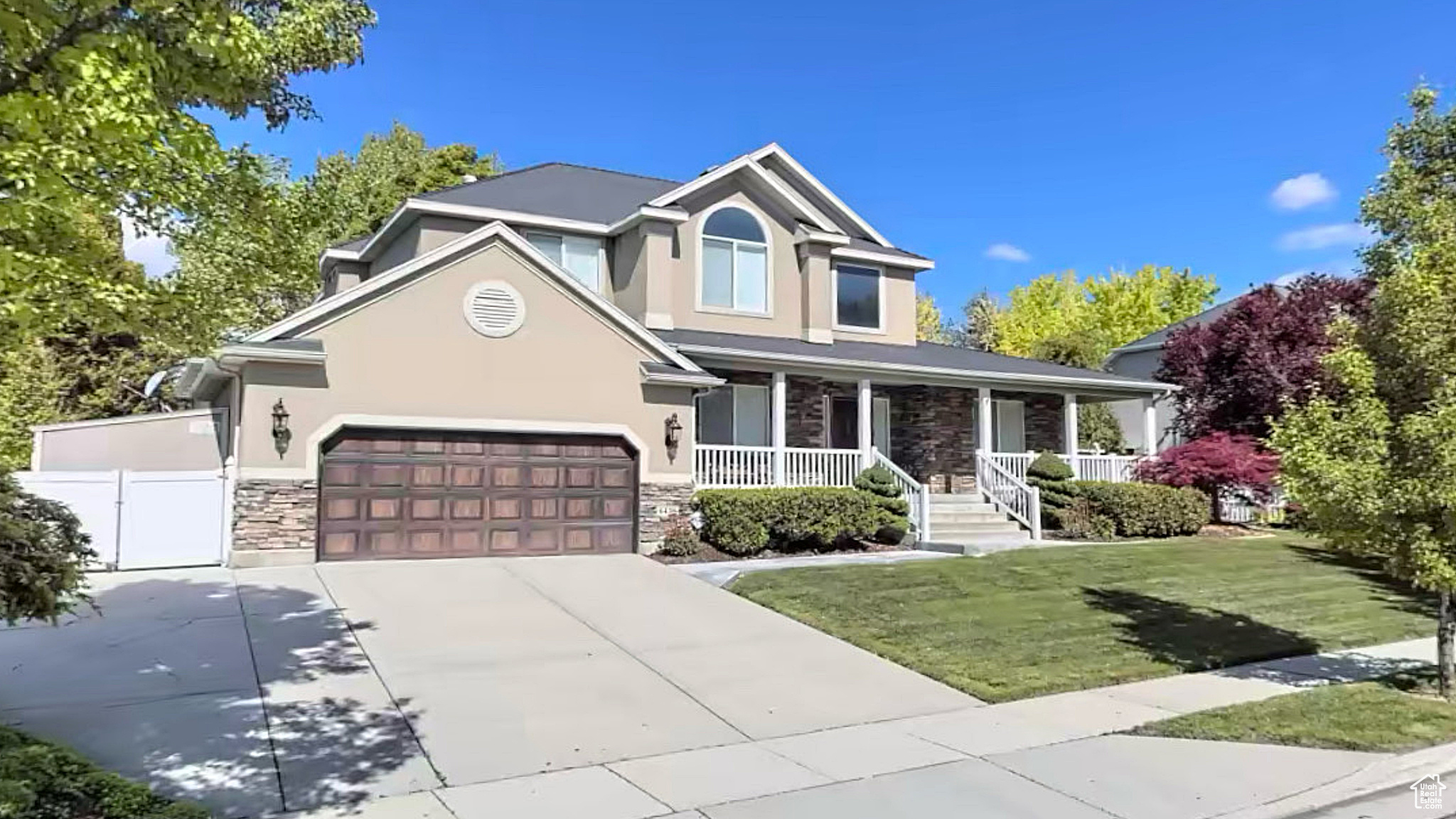 View of front of home with covered porch, a garage, stone siding, driveway, and stucco siding