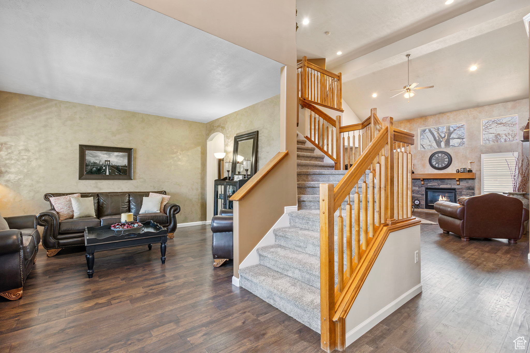 Staircase with ceiling fan, wood-type flooring, a stone fireplace, and lofted ceiling with beams