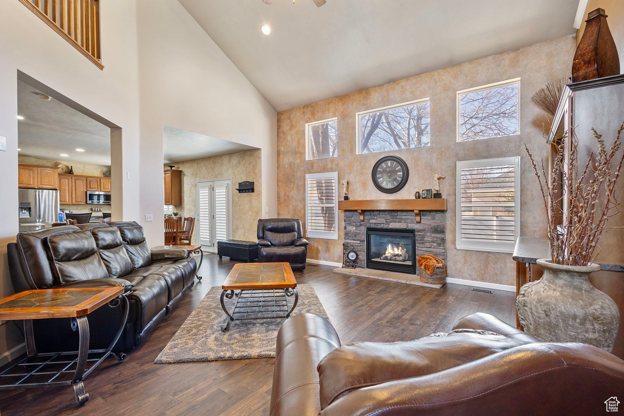 Living room with a stone fireplace, high vaulted ceiling, dark hardwood / wood-style flooring, and plenty of natural light