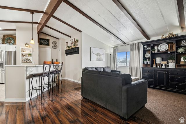 Living area with vaulted ceiling with beams, baseboards, and dark wood finished floors