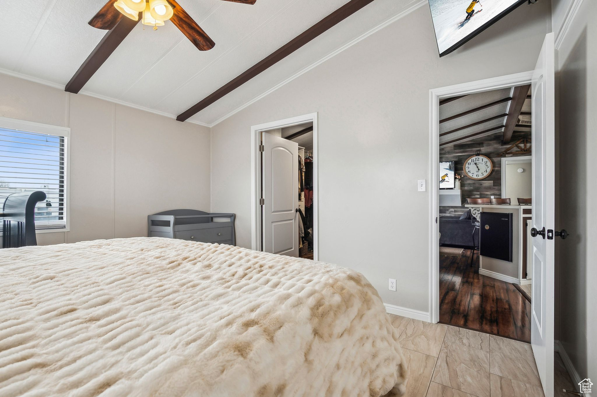 Bedroom featuring lofted ceiling with beams, crown molding, a walk in closet, and a ceiling fan