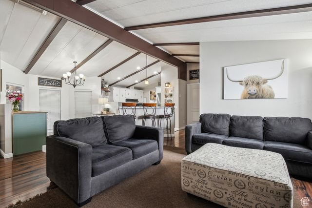 Living area featuring lofted ceiling with beams, dark wood-style floors, baseboards, and a notable chandelier