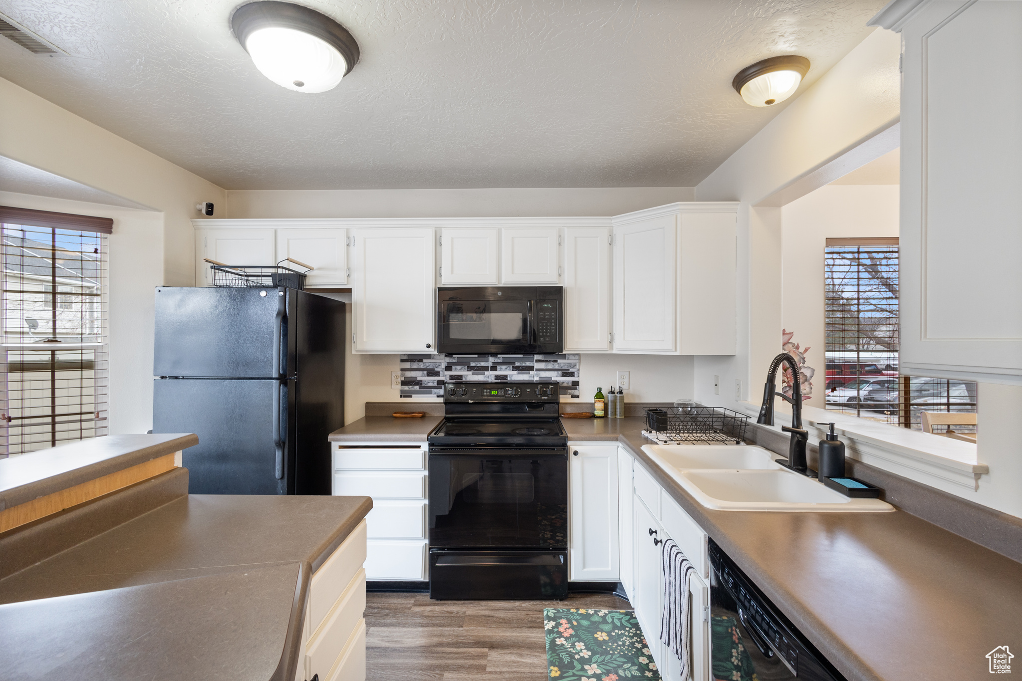 Kitchen with sink, black appliances, light hardwood / wood-style floors, decorative backsplash, and white cabinets