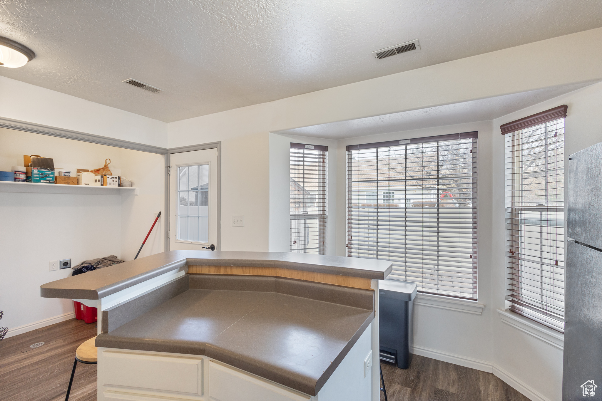 Kitchen with black fridge, dark hardwood / wood-style flooring, and a textured ceiling