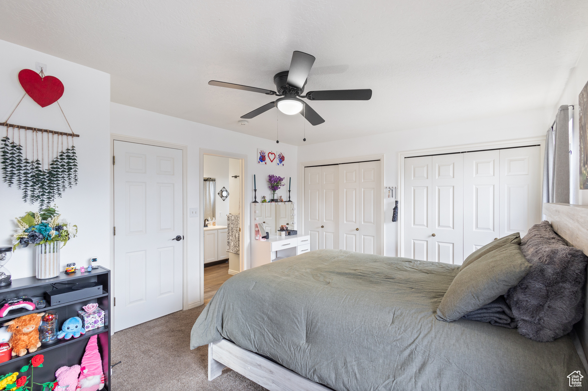 Carpeted bedroom with two closets, ceiling fan, and ensuite bathroom