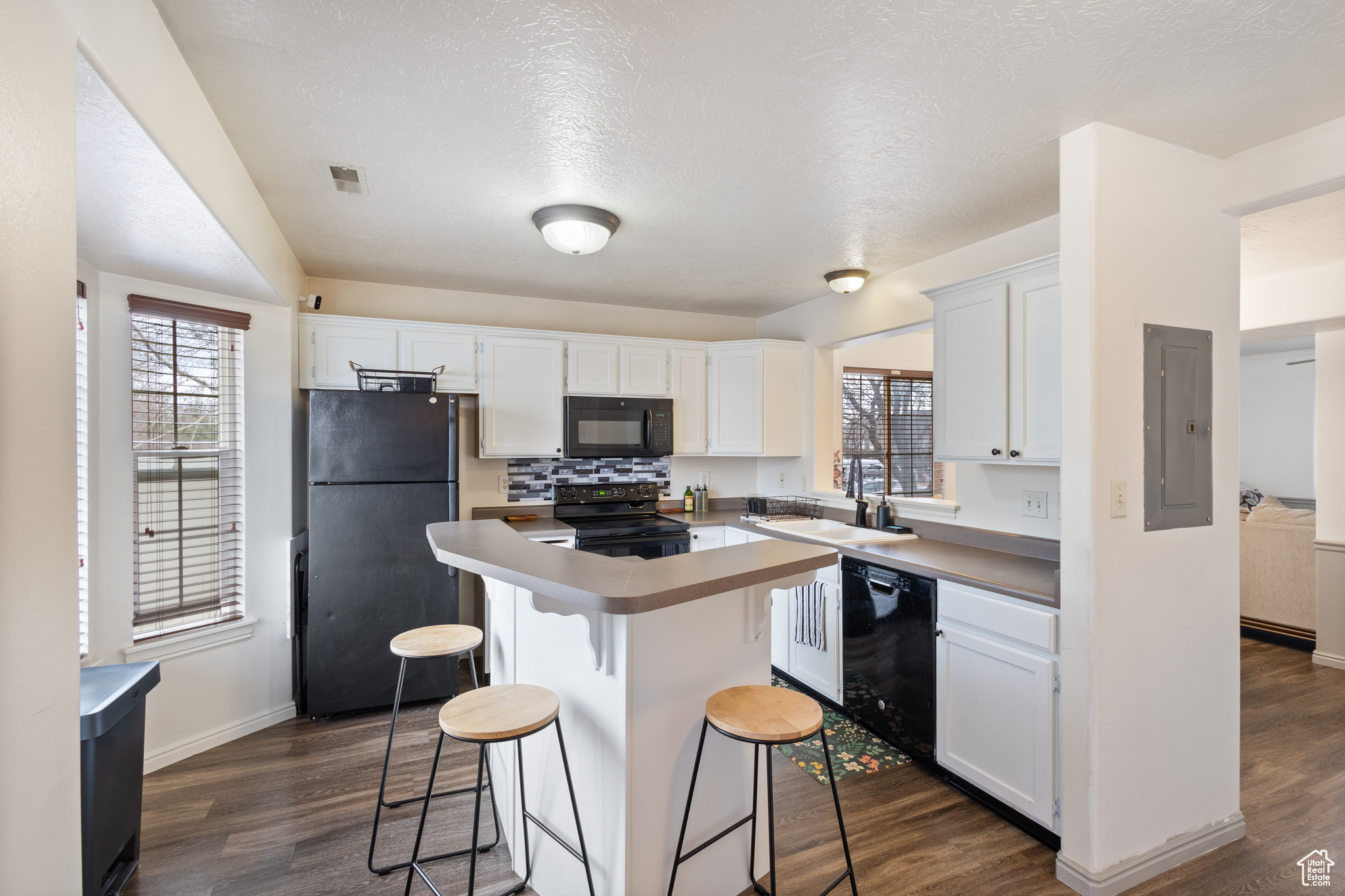 Kitchen featuring dark wood-type flooring, white cabinetry, electric panel, a center island, and black appliances