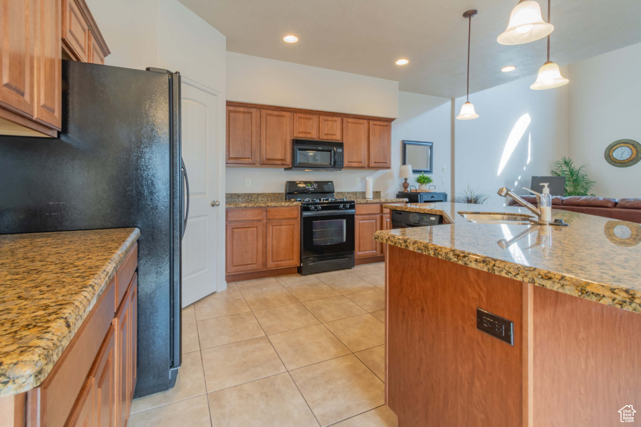 Kitchen featuring light tile patterned floors, a sink, hanging light fixtures, brown cabinets, and black appliances