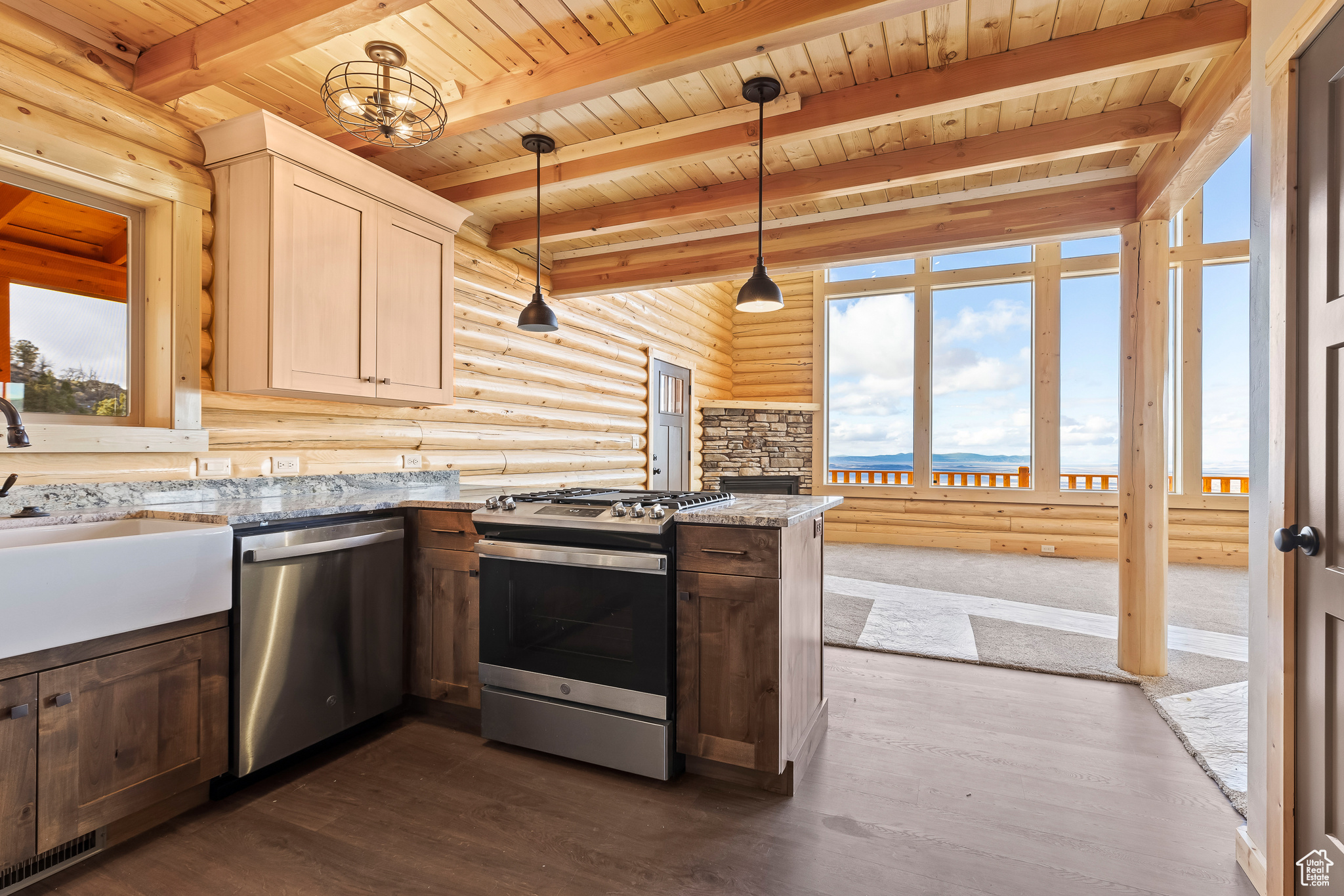 Kitchen featuring dark wood-style floors, appliances with stainless steel finishes, light stone countertops, pendant lighting, and a sink