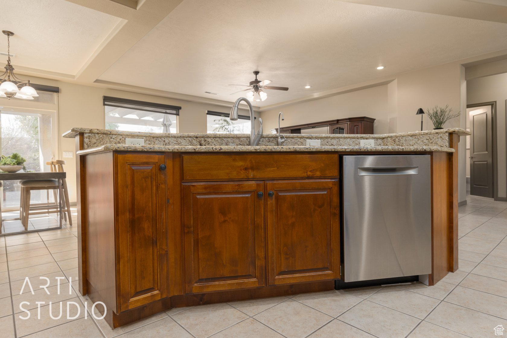 Kitchen with light tile patterned flooring, stainless steel dishwasher, decorative light fixtures, and light stone countertops