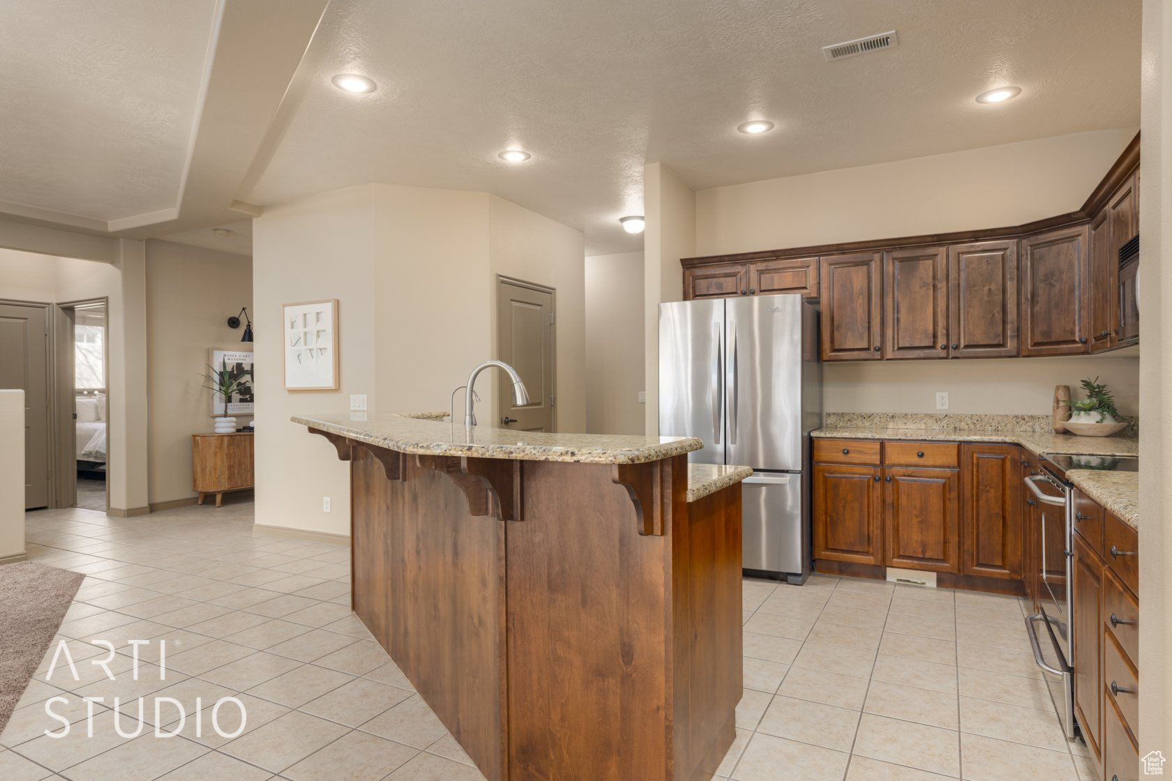 Kitchen featuring appliances with stainless steel finishes, a kitchen island with sink, light tile patterned floors, and a breakfast bar