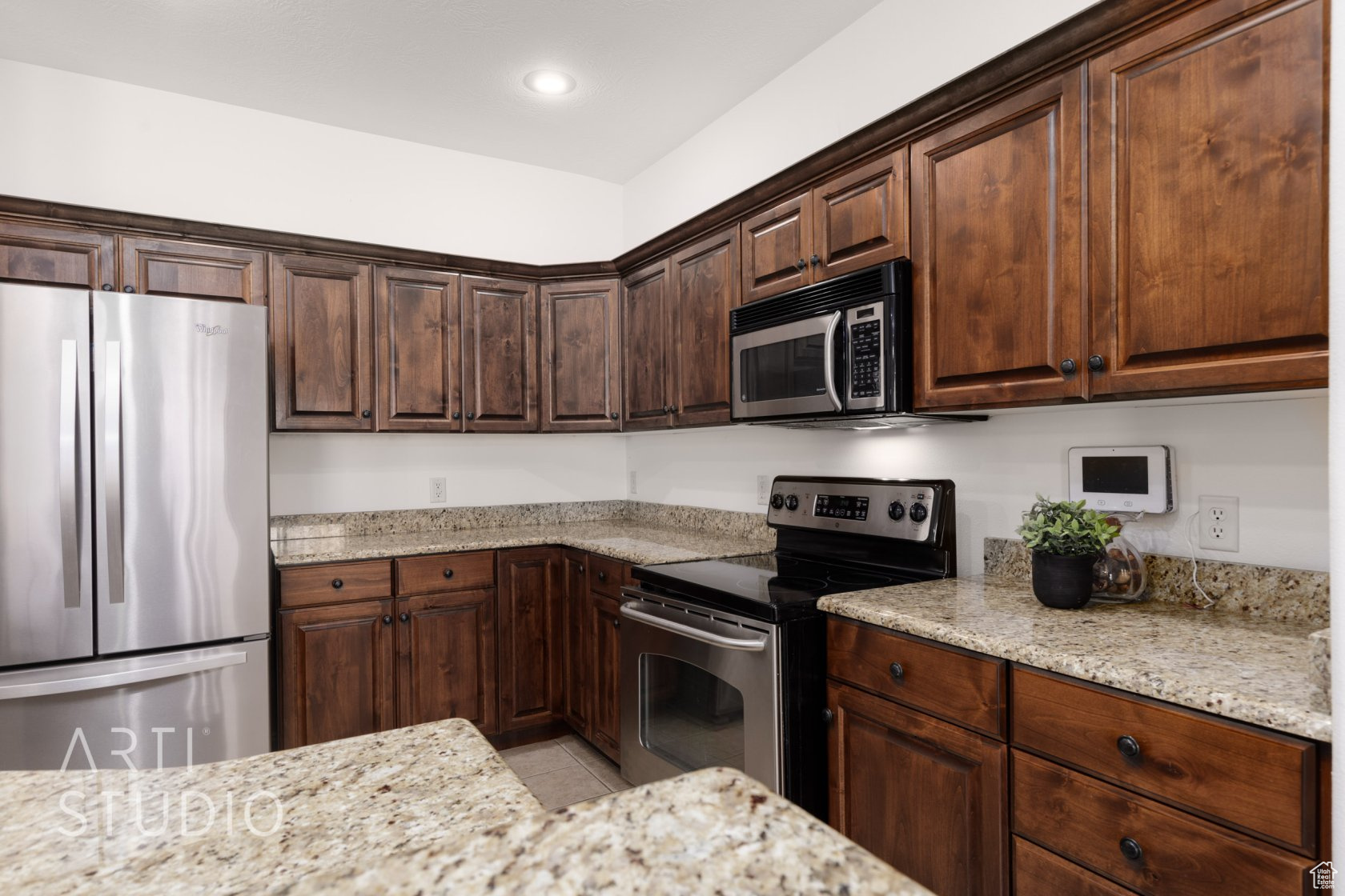 Kitchen with appliances with stainless steel finishes, dark brown cabinets, and light stone counters
