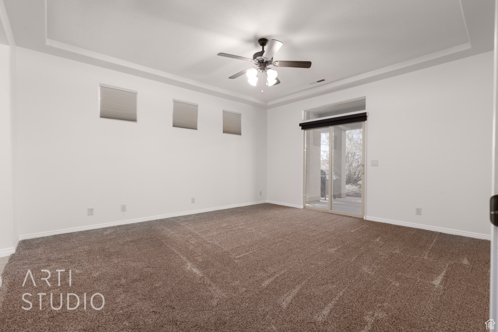 Spare room with a raised ceiling, ceiling fan, and dark colored carpet