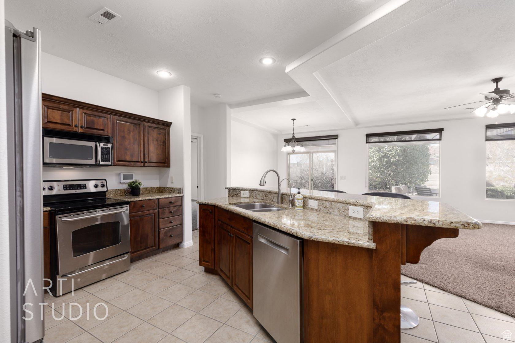 Kitchen with an island with sink, sink, hanging light fixtures, stainless steel appliances, and light stone countertops