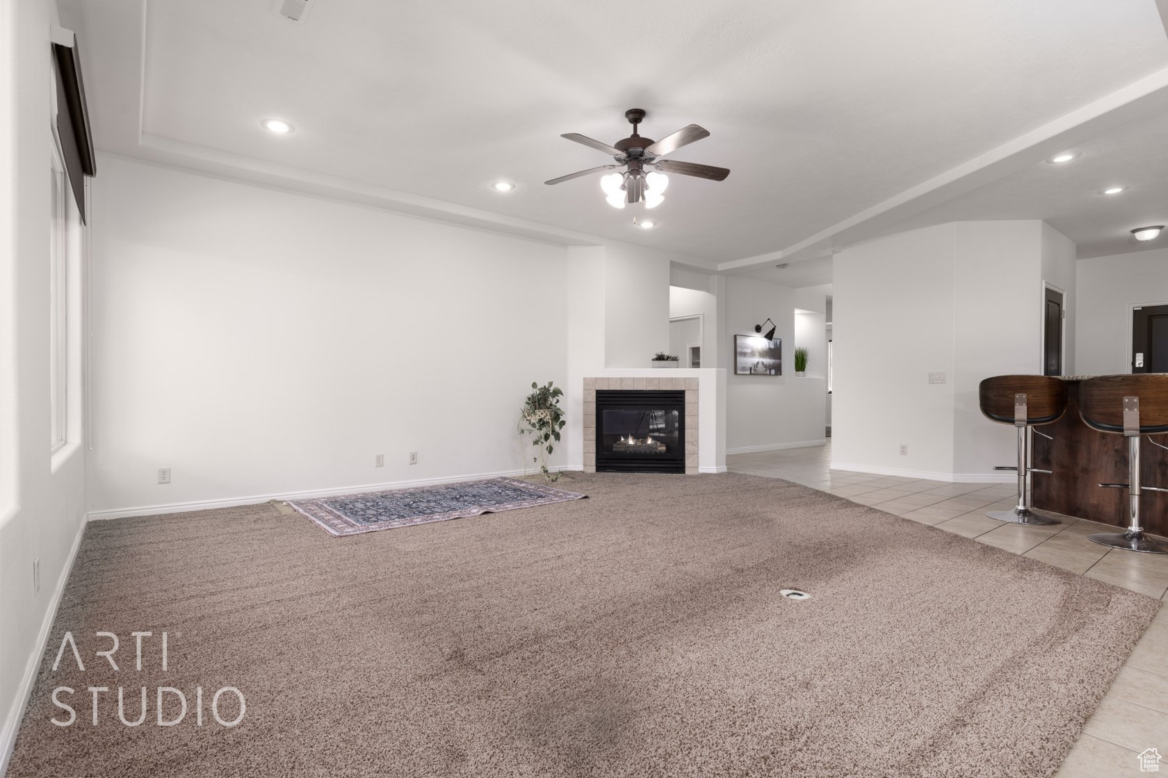 Unfurnished living room featuring light tile patterned flooring, ceiling fan, indoor bar, and a tile fireplace